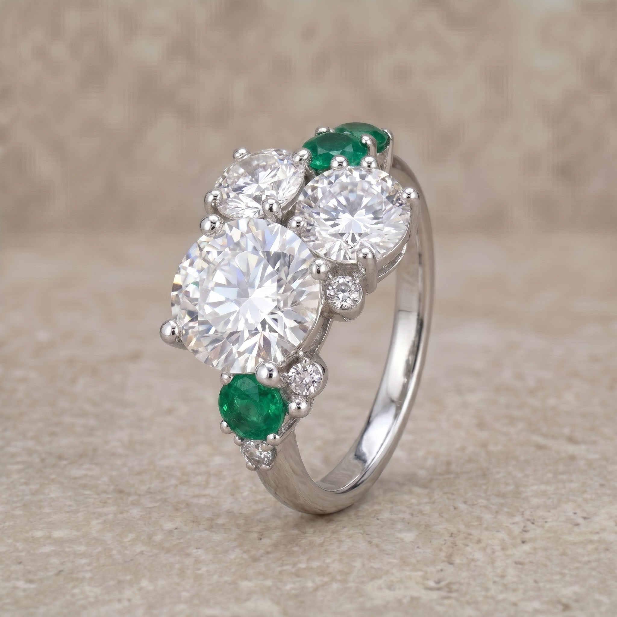 Silver ring with large central gem, smaller gems, and emeralds on a beige background