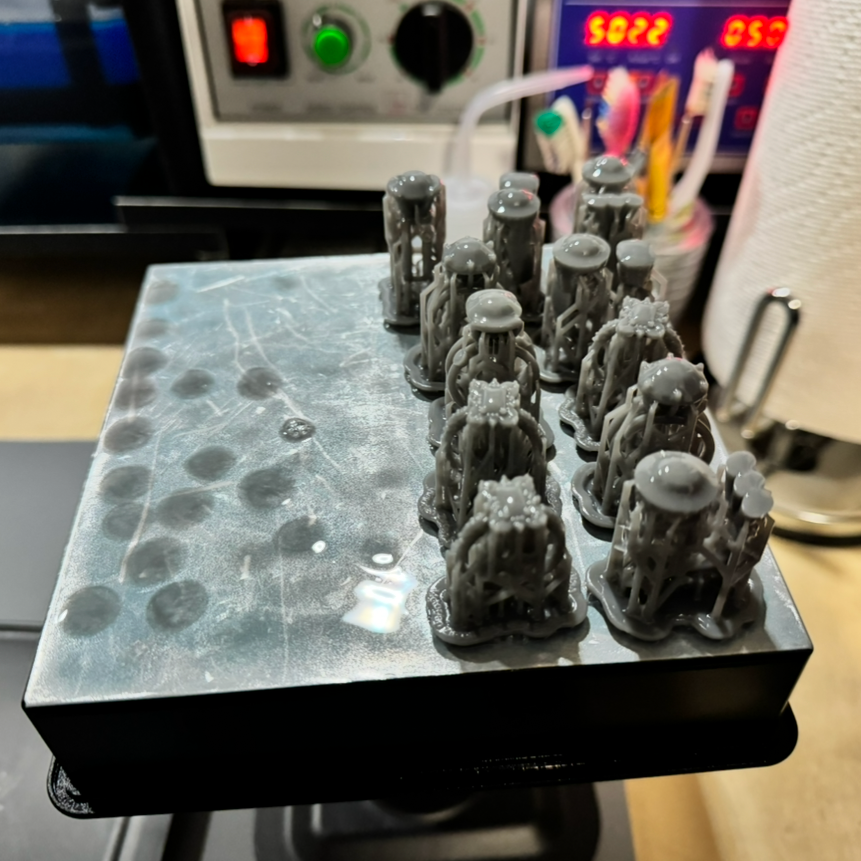 3D-printed jewelry pieces on a build platform with a blurred indoor background