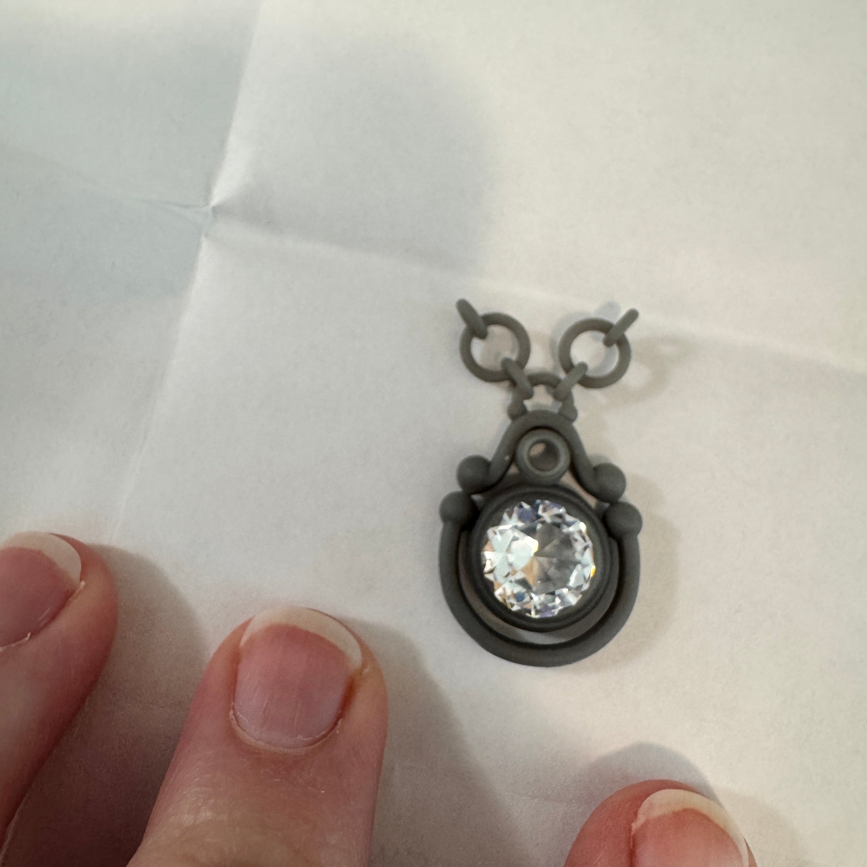 3d Printed prototype with a gemstone held between fingers on a white background
