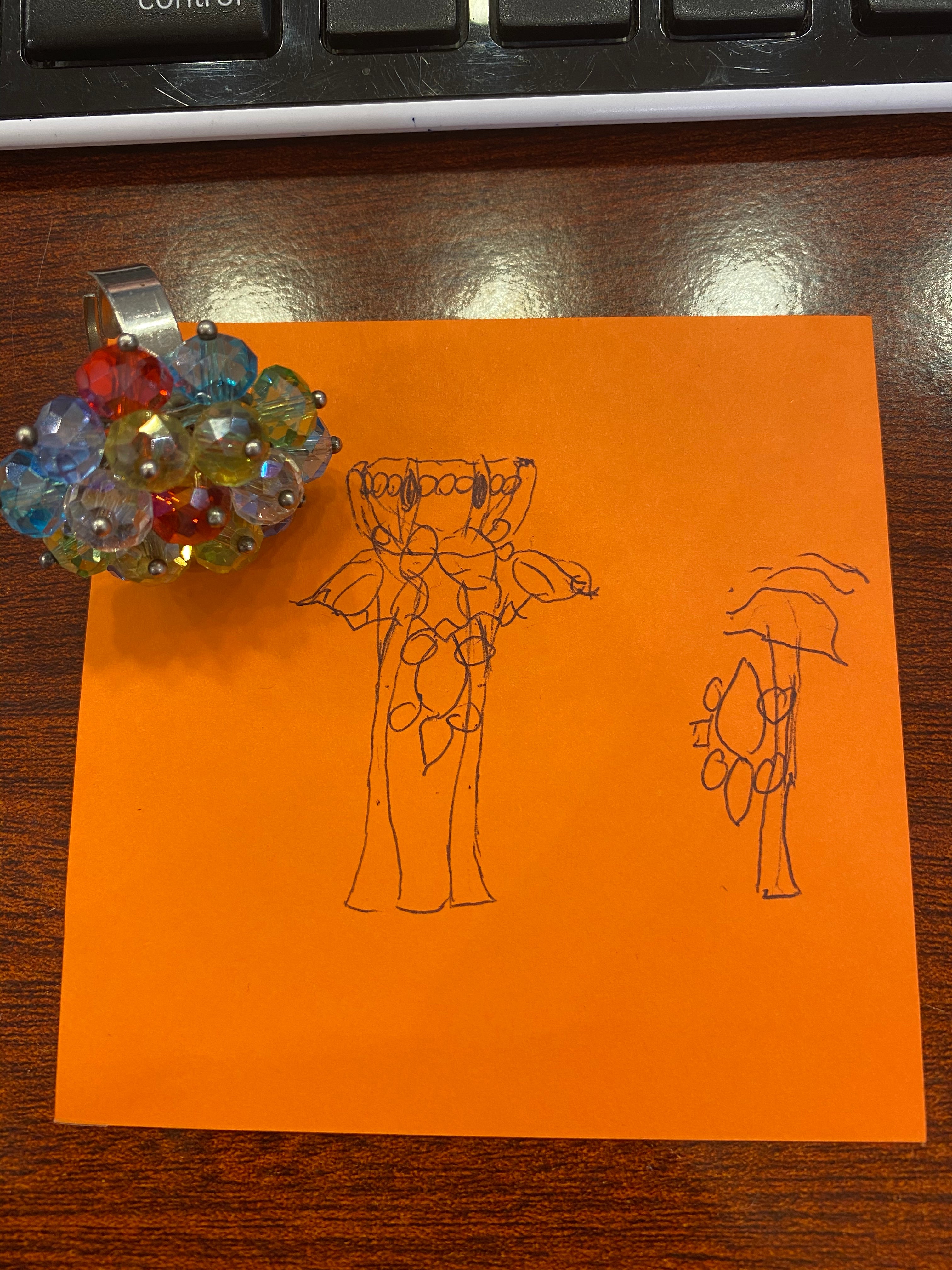 Orange paper with a jewelry sketch a pile of colorful beads on a wooden surface.