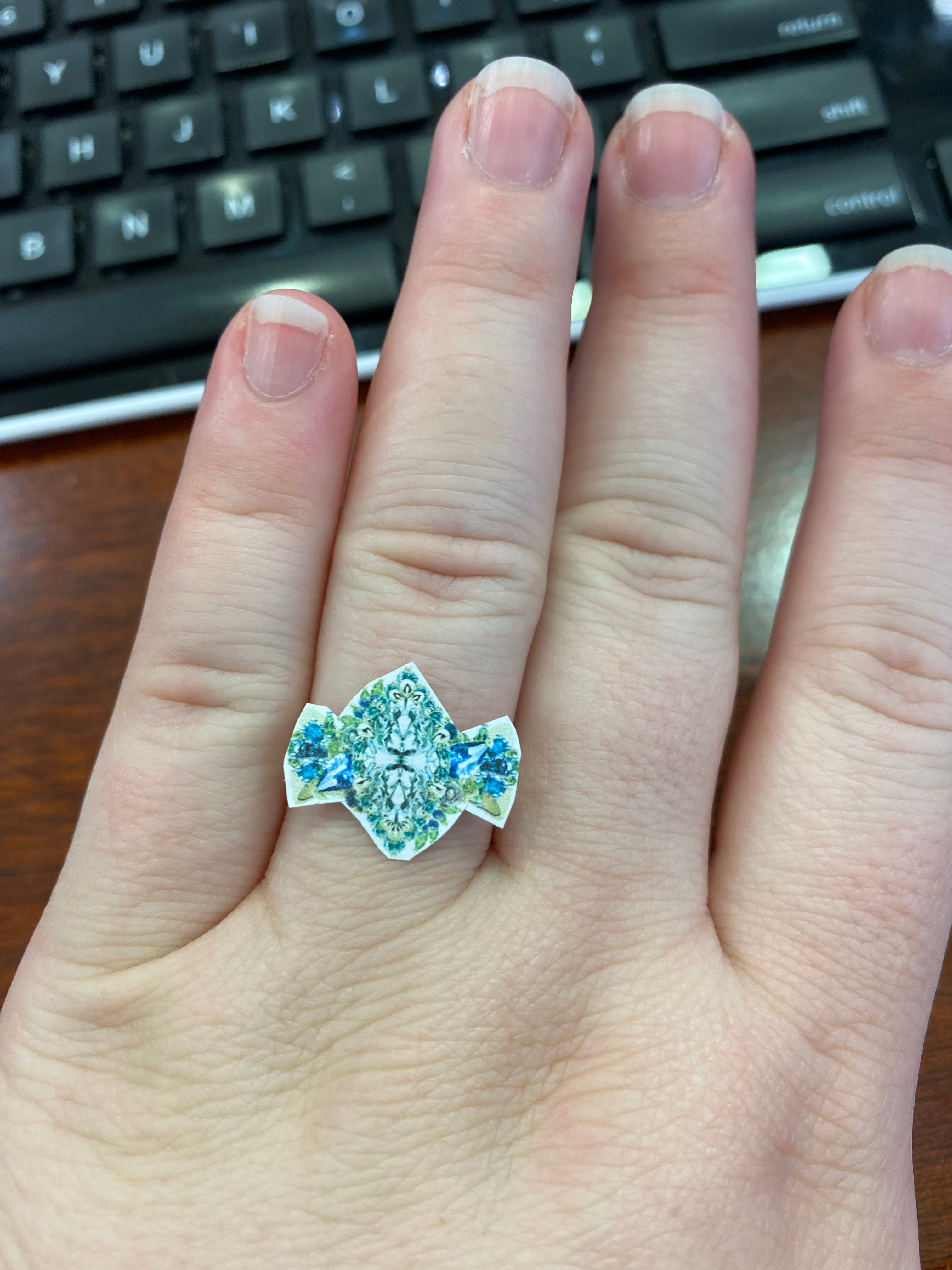 Hand wearing a paper prototype of a decorative ring with gemstones in front of a keyboard