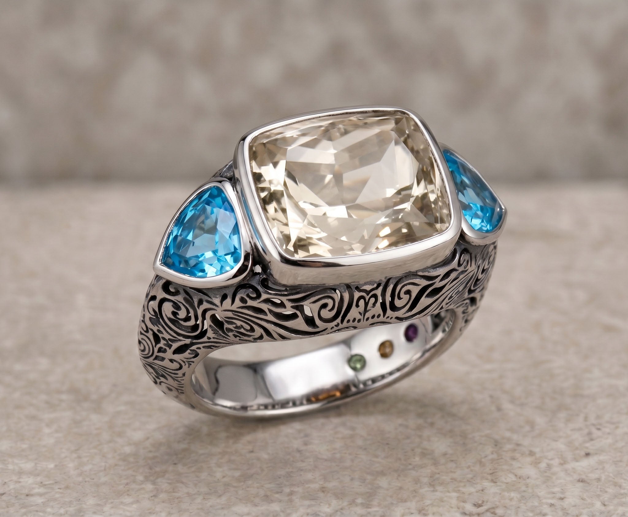 Silver ring with a large central gemstone and smaller blue stones on a textured surface