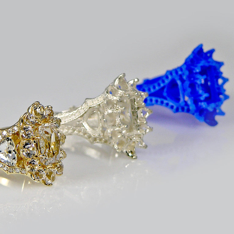 Two diamond rings, one gold and one silver, with a blue 3D-printed object on a light gray background.